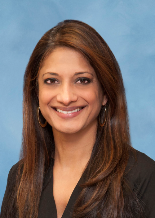 Dr. Sarma is pictured wearing a black blouse and gold hoop earrings.